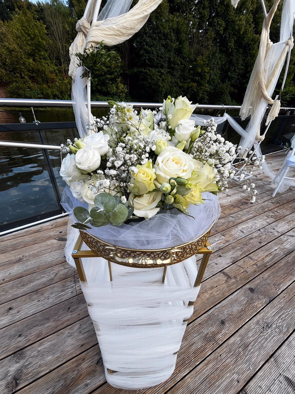 Weißes Bouquet aus Rose, Lisianthus und Schleierkraut auf goldener Säule am Wasser.