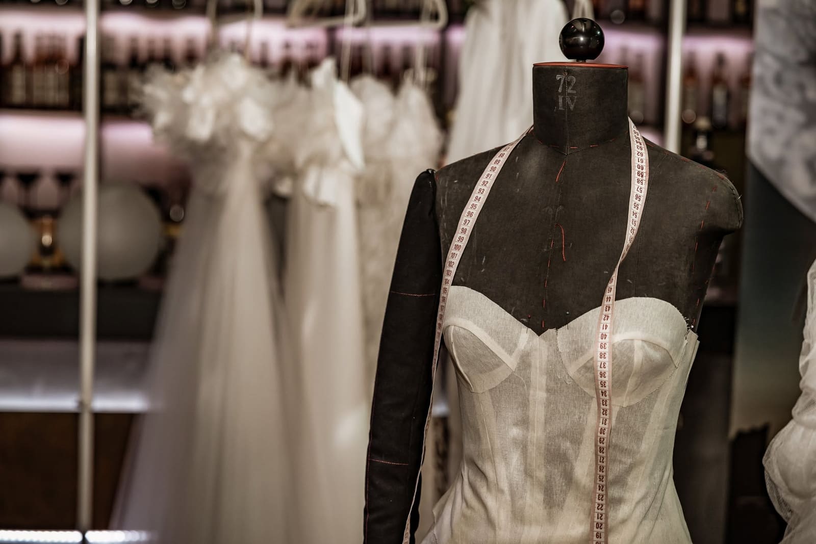 Brautkleid in Arbeit auf einer Schneiderpuppe mit Maßband, im Hintergrund weitere Kleider